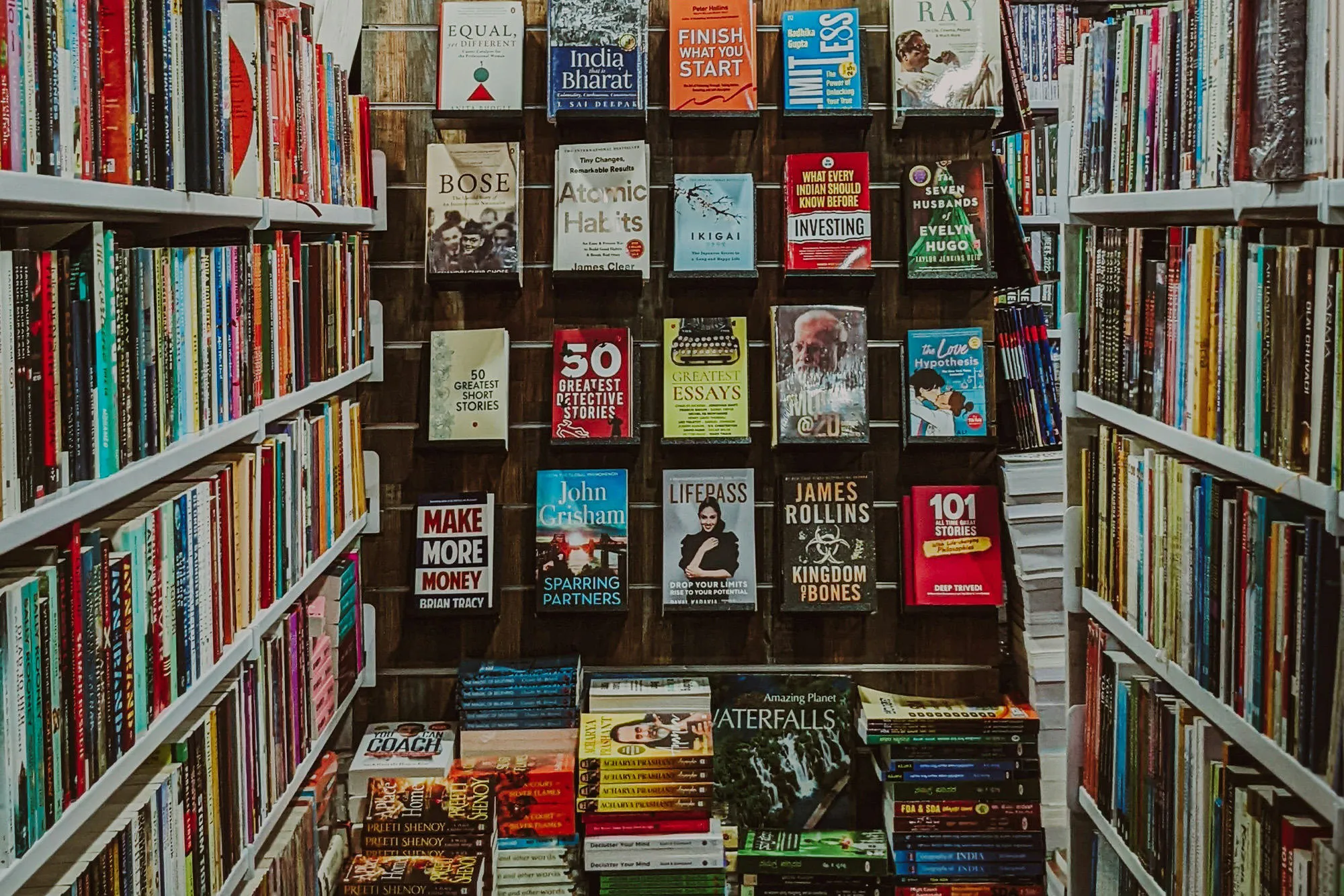 An aisle in a library packed with books on the shelves and in a display at the end.